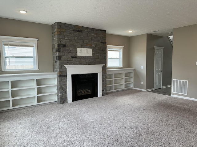 unfurnished living room with a stone fireplace, carpet, and a textured ceiling