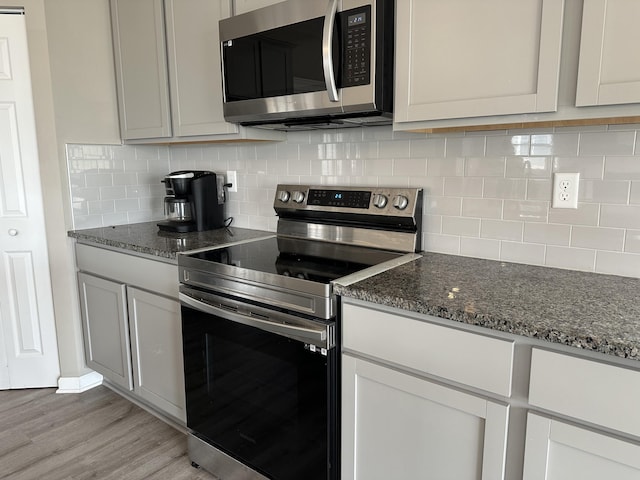 kitchen featuring light wood-type flooring, stainless steel appliances, dark stone counters, and backsplash