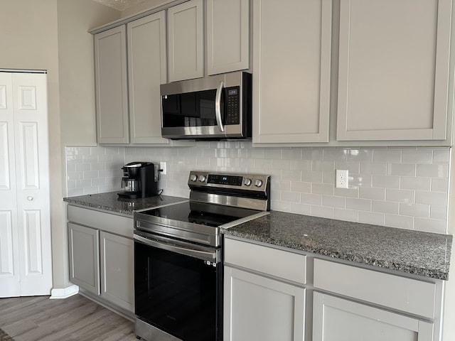 kitchen featuring dark stone counters, decorative backsplash, stainless steel appliances, and light hardwood / wood-style floors