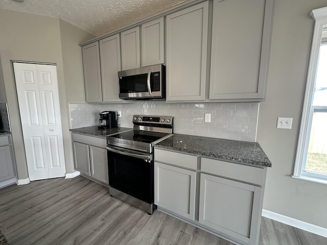 kitchen with gray cabinetry, backsplash, light wood-type flooring, a textured ceiling, and stainless steel appliances