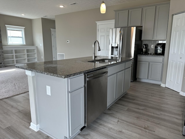 kitchen featuring sink, a textured ceiling, gray cabinets, a center island with sink, and appliances with stainless steel finishes