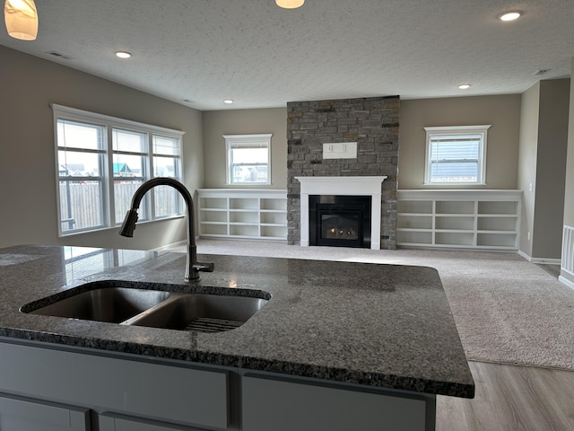 kitchen featuring a stone fireplace, sink, a textured ceiling, and light hardwood / wood-style flooring