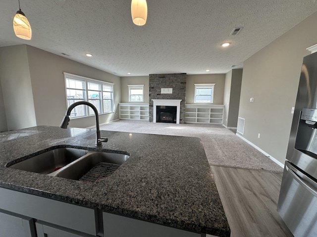 kitchen with pendant lighting, a stone fireplace, sink, hardwood / wood-style flooring, and a textured ceiling