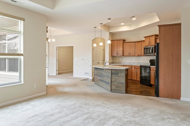 kitchen with black appliances, decorative light fixtures, a center island with sink, and light carpet