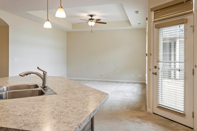 kitchen featuring carpet, a raised ceiling, ceiling fan, sink, and hanging light fixtures