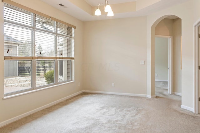 empty room with carpet, a tray ceiling, and a notable chandelier