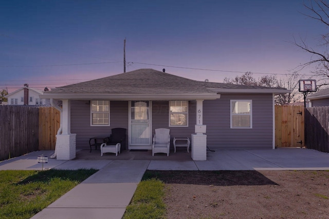 bungalow-style home with covered porch, roof with shingles, and fence