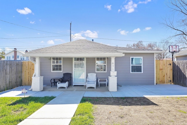 bungalow with covered porch, roof with shingles, and fence