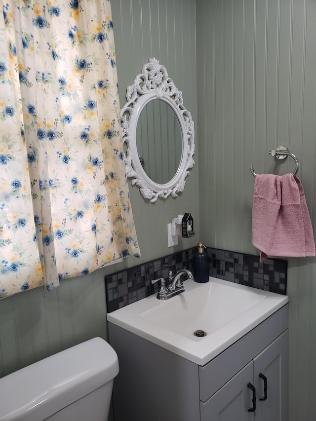 bathroom with tasteful backsplash, wood walls, vanity, and toilet