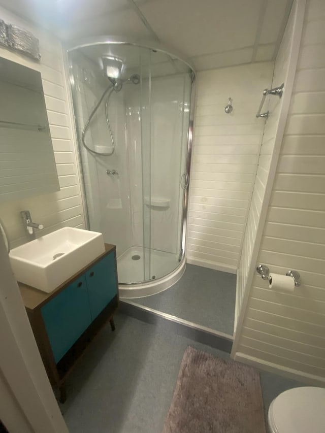 bathroom with vanity, toilet, an enclosed shower, and wood walls