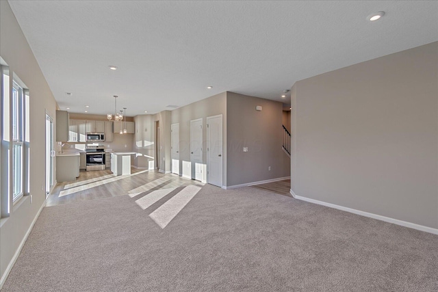 unfurnished living room featuring sink, light colored carpet, a textured ceiling, and a notable chandelier