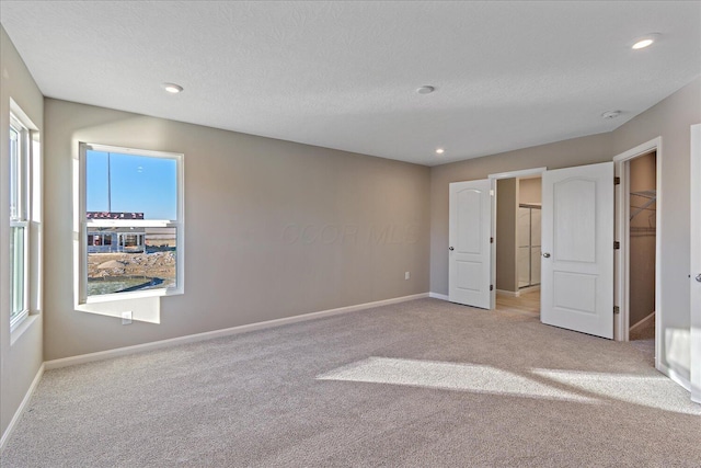 unfurnished bedroom with light carpet, a textured ceiling, a walk in closet, and a closet