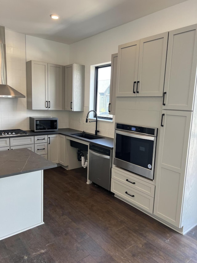 kitchen featuring sink, wall chimney exhaust hood, tasteful backsplash, dark hardwood / wood-style flooring, and appliances with stainless steel finishes