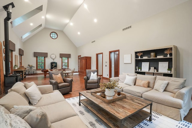 living room with a wood stove, light hardwood / wood-style flooring, and high vaulted ceiling