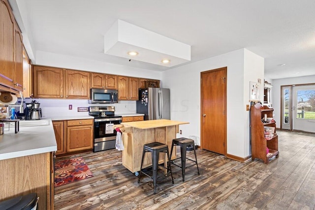 kitchen featuring a kitchen breakfast bar, stainless steel appliances, a kitchen island, and dark wood-type flooring