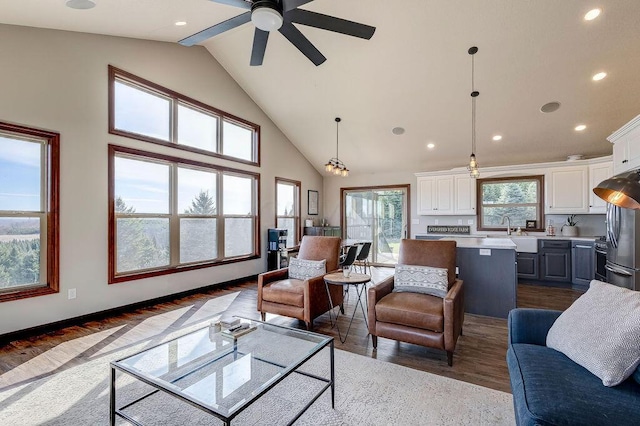 living room featuring a wealth of natural light, high vaulted ceiling, ceiling fan with notable chandelier, and dark hardwood / wood-style floors