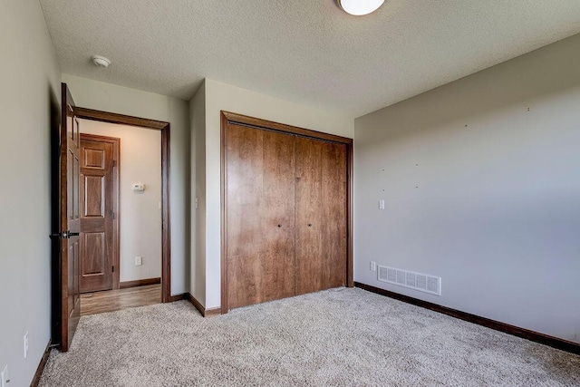 unfurnished bedroom featuring a textured ceiling, light carpet, and a closet