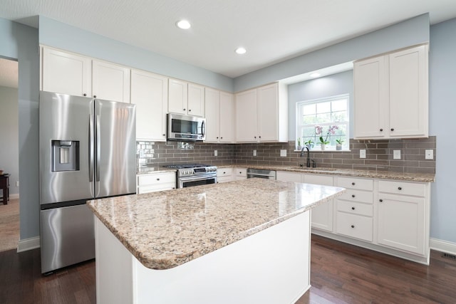 kitchen with stainless steel appliances, white cabinets, a kitchen island, and light stone countertops