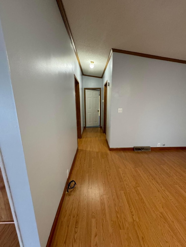 hall with a textured ceiling, lofted ceiling, crown molding, and light hardwood / wood-style flooring