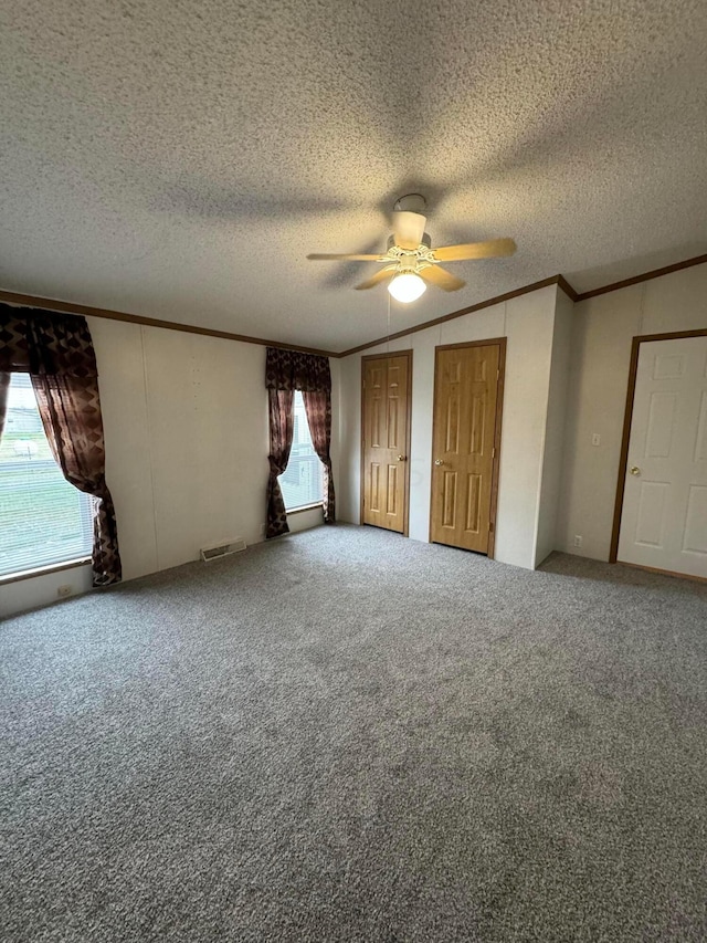 unfurnished bedroom featuring multiple closets, ceiling fan, a textured ceiling, carpet, and ornamental molding