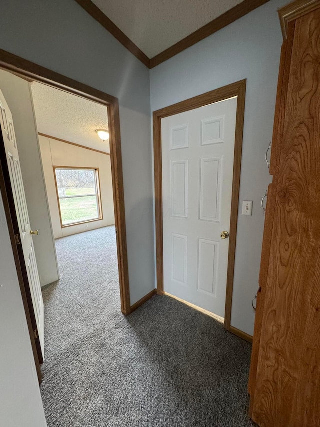 corridor with dark colored carpet, ornamental molding, a textured ceiling, and vaulted ceiling