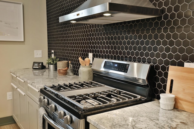 kitchen with gas stove, light stone countertops, and wall chimney range hood