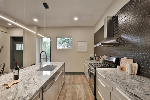 kitchen with hanging light fixtures, wall chimney exhaust hood, light wood-type flooring, white cabinetry, and stainless steel appliances