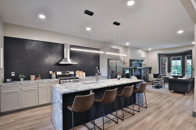 kitchen featuring appliances with stainless steel finishes, decorative light fixtures, a kitchen island with sink, and wall chimney range hood