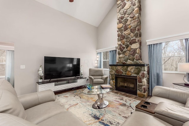 living room featuring a stone fireplace, high vaulted ceiling, a healthy amount of sunlight, and wood-type flooring