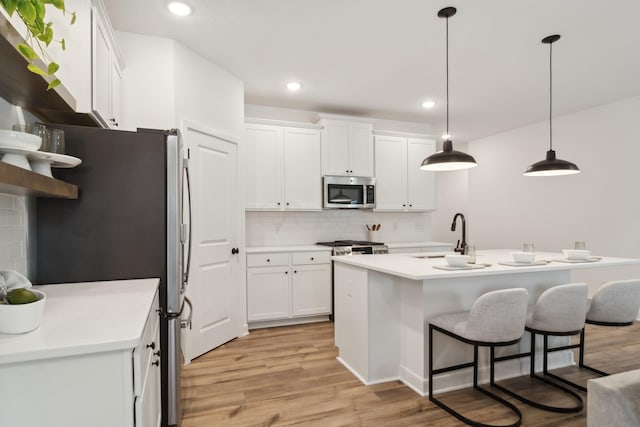 kitchen with white cabinetry, sink, light hardwood / wood-style flooring, decorative light fixtures, and appliances with stainless steel finishes