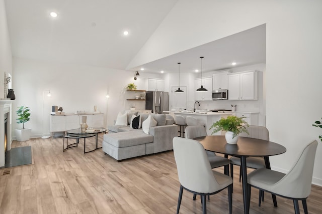 dining area featuring sink, high vaulted ceiling, and light wood-type flooring