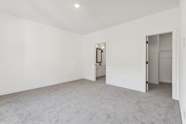 unfurnished bedroom featuring a walk in closet, connected bathroom, light colored carpet, and a closet