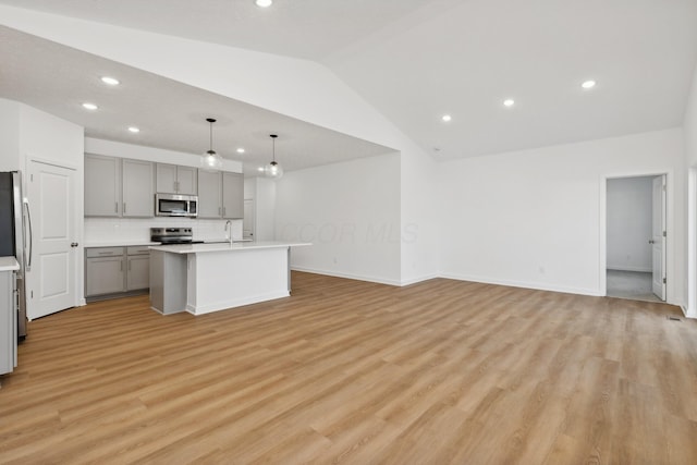 kitchen with appliances with stainless steel finishes, gray cabinets, hanging light fixtures, lofted ceiling, and an island with sink