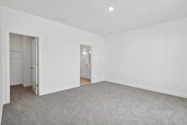 unfurnished bedroom with a closet, a spacious closet, carpet floors, and ensuite bath