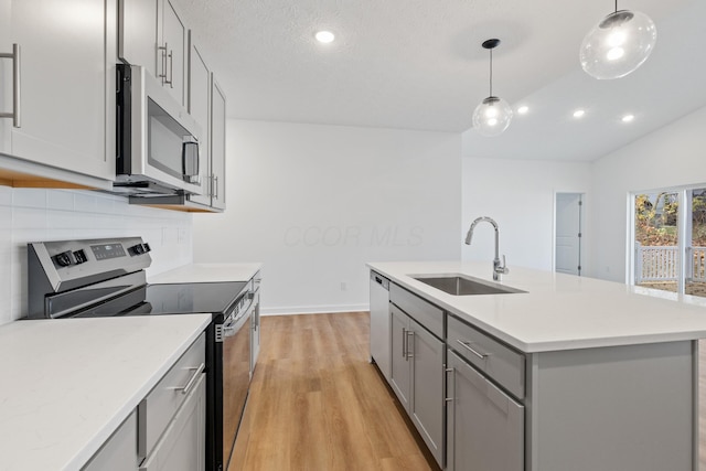 kitchen with sink, decorative light fixtures, gray cabinets, a kitchen island with sink, and appliances with stainless steel finishes