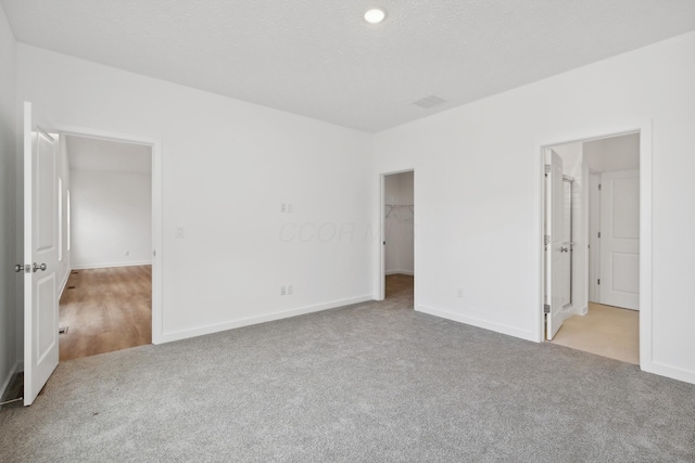 unfurnished bedroom with light carpet, a walk in closet, ensuite bath, and a closet