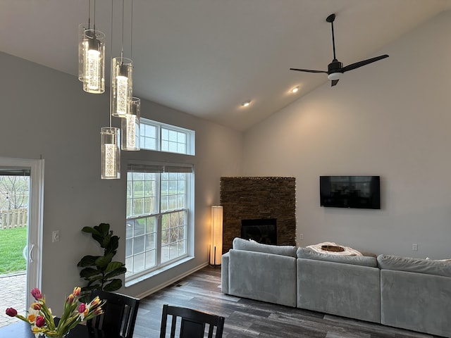 living room featuring dark hardwood / wood-style floors, a stone fireplace, ceiling fan, and a healthy amount of sunlight