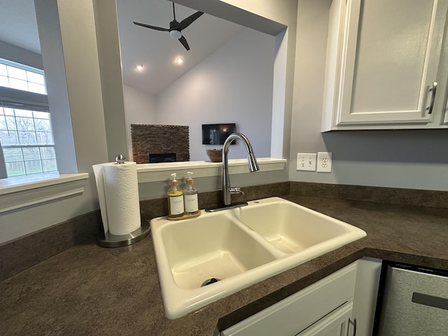 interior details featuring white cabinets, ceiling fan, sink, dishwasher, and a fireplace