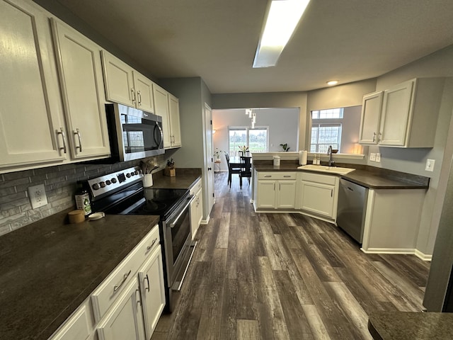 kitchen featuring kitchen peninsula, appliances with stainless steel finishes, dark hardwood / wood-style flooring, sink, and a chandelier