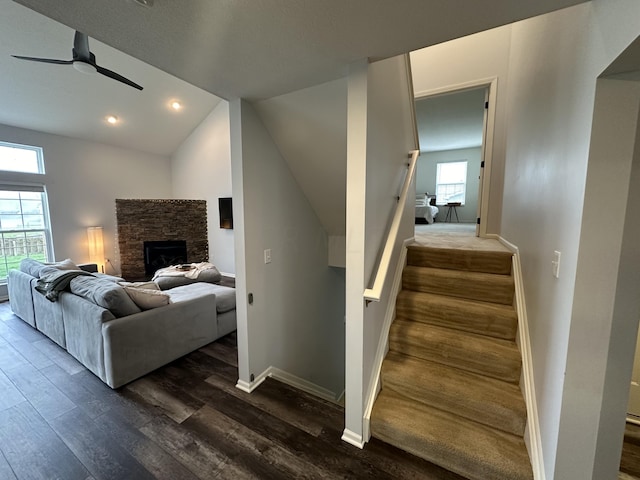 stairway with a stone fireplace, ceiling fan, hardwood / wood-style floors, and vaulted ceiling