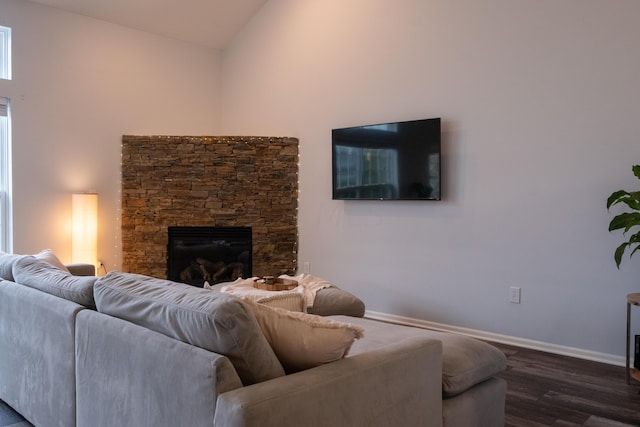 living room featuring dark hardwood / wood-style flooring, high vaulted ceiling, and a stone fireplace