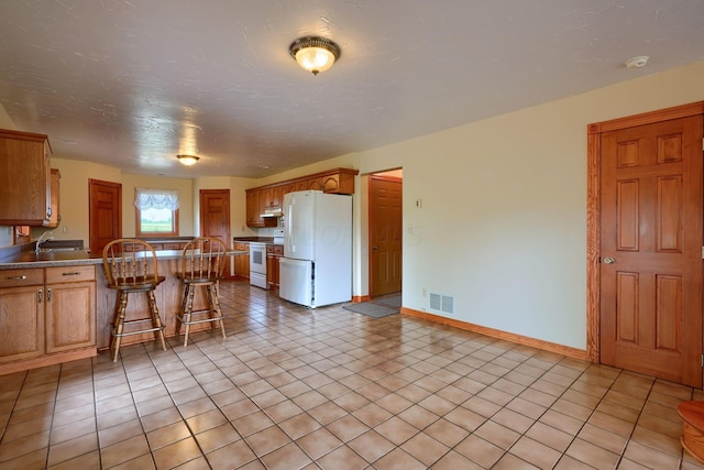 kitchen featuring a kitchen breakfast bar, light tile patterned floors, and white appliances