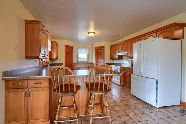 kitchen featuring a textured ceiling, a kitchen bar, light tile patterned flooring, and white appliances