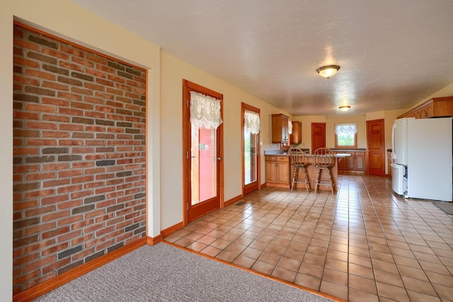 kitchen featuring kitchen peninsula, a textured ceiling, white refrigerator, a breakfast bar area, and light tile patterned flooring