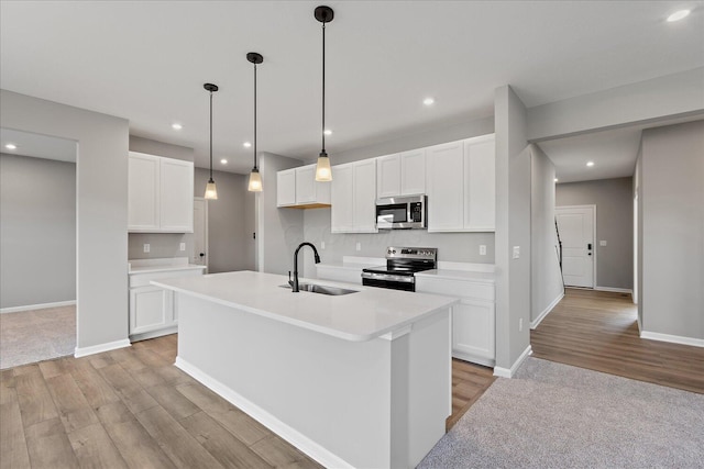 kitchen with stainless steel appliances, sink, light hardwood / wood-style floors, white cabinetry, and an island with sink