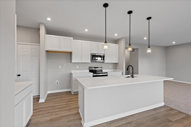 kitchen with appliances with stainless steel finishes, sink, pendant lighting, white cabinetry, and an island with sink