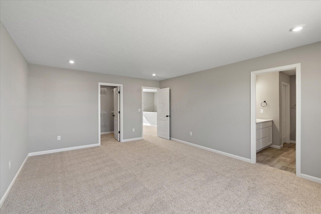 unfurnished bedroom with ensuite bath, a spacious closet, light colored carpet, and a textured ceiling