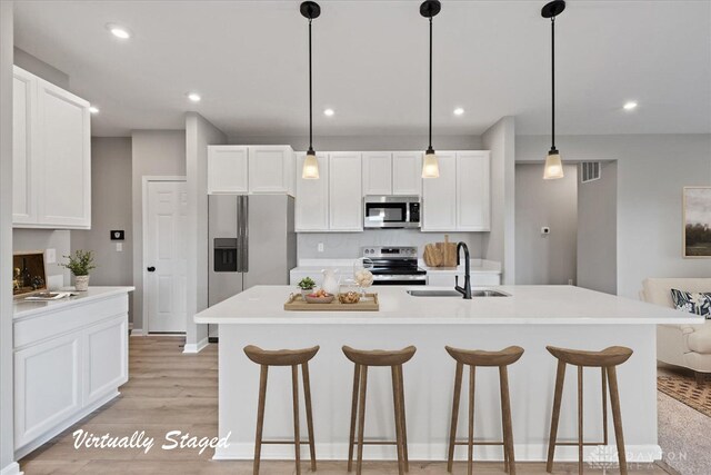 kitchen with a kitchen island with sink, sink, hanging light fixtures, and appliances with stainless steel finishes