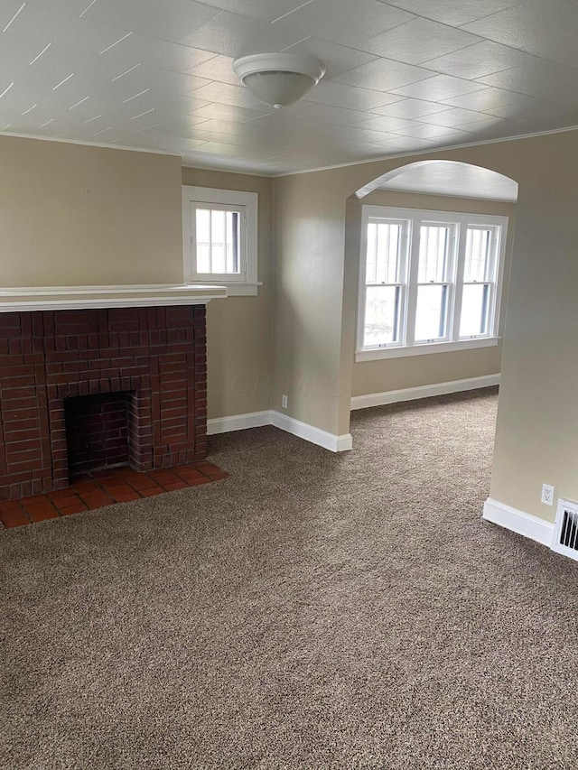 unfurnished living room with a fireplace, a healthy amount of sunlight, and dark colored carpet