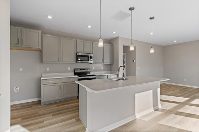 kitchen with pendant lighting, a center island with sink, sink, gray cabinets, and appliances with stainless steel finishes